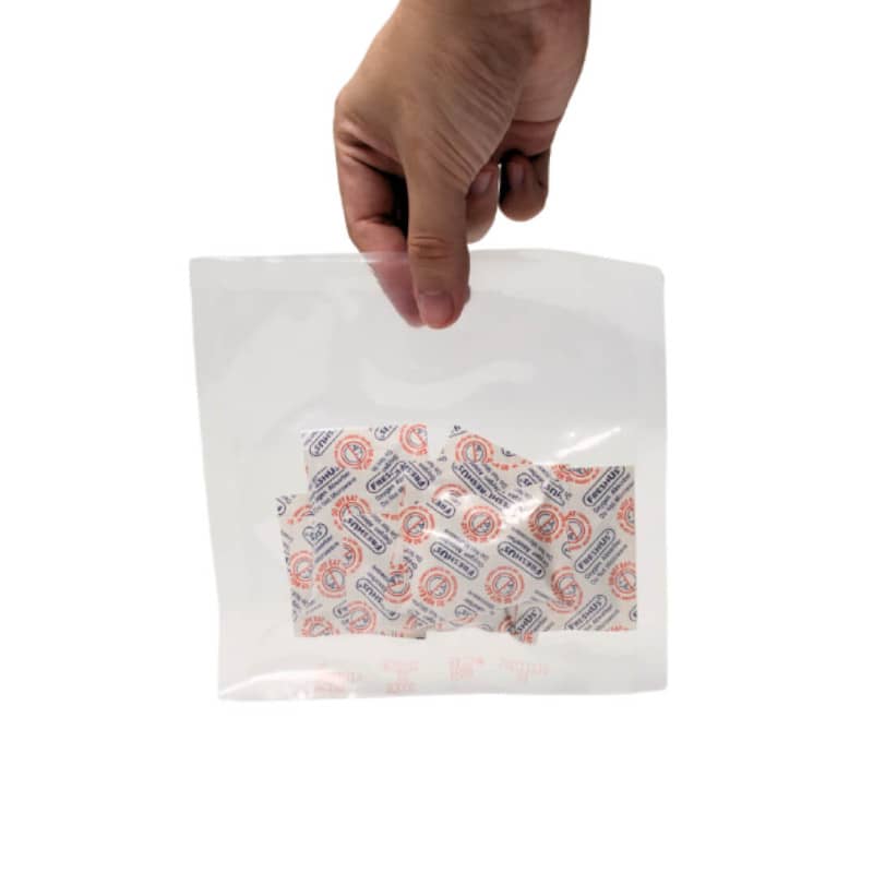 Hand holding a white packet of oxygen absorbers with a clear window showing the contents