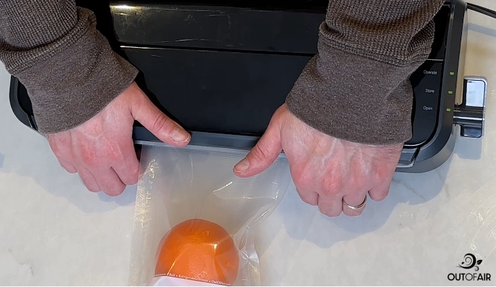 Hand pressing down on a vacuum sealer lid while the motor runs